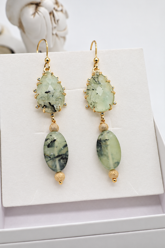Orecchini pendenti in prehnite con pietre verdi ovali lisce, cabochon sfaccettati e dettagli dorati, presentati in confezione regalo.