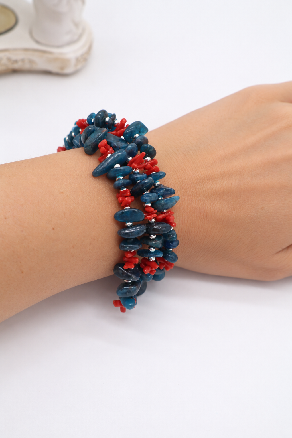 Bracciale a tre fili in apatite blu e corallo rosso indossato al polso con dettagli in argento rodiato