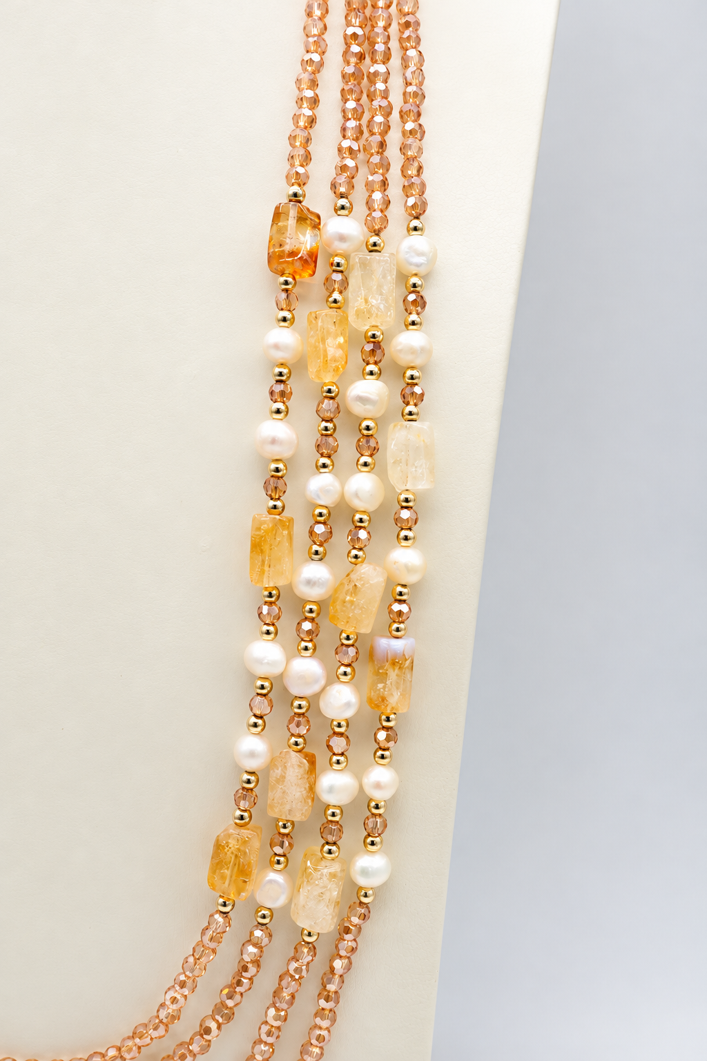 Collana multifilo da 90 cm con cinque fili di cristalli sfaccettati color champagne da 3 mm, citrino rettangolare da 14 × 10 mm, perle semi-round da 5 mm e distanziatori dorati.