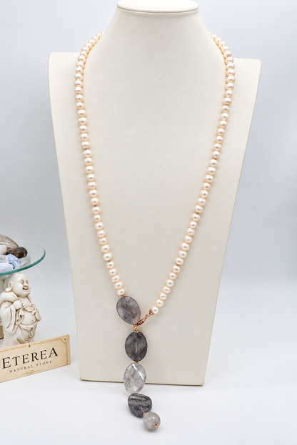 Collana lunga in perle di fiume e quarzo grigio sfaccettato con chiusura in argento rosé, indossata con abito color avorio.