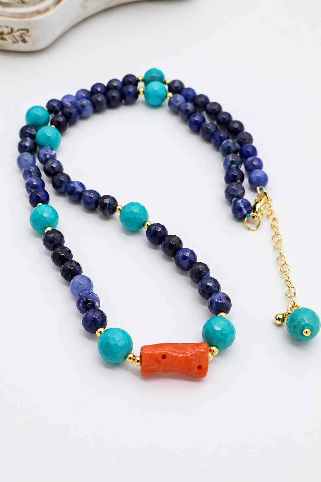 Dettaglio della collana Nefertari con perle di sodalite blu, turchese sfaccettato e elemento centrale in corallo mediterraneo