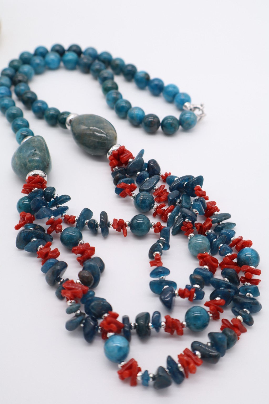 Collana lunga 75 cm in apatite e corallo rosso disposta su piano bianco, vista della struttura a tre fili