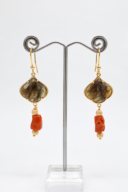 Coppia di orecchini pendenti in labradorite e corallo mediterraneo esposti su un supporto per gioielli, con monachelle in argento 925 dorato e design allungato.