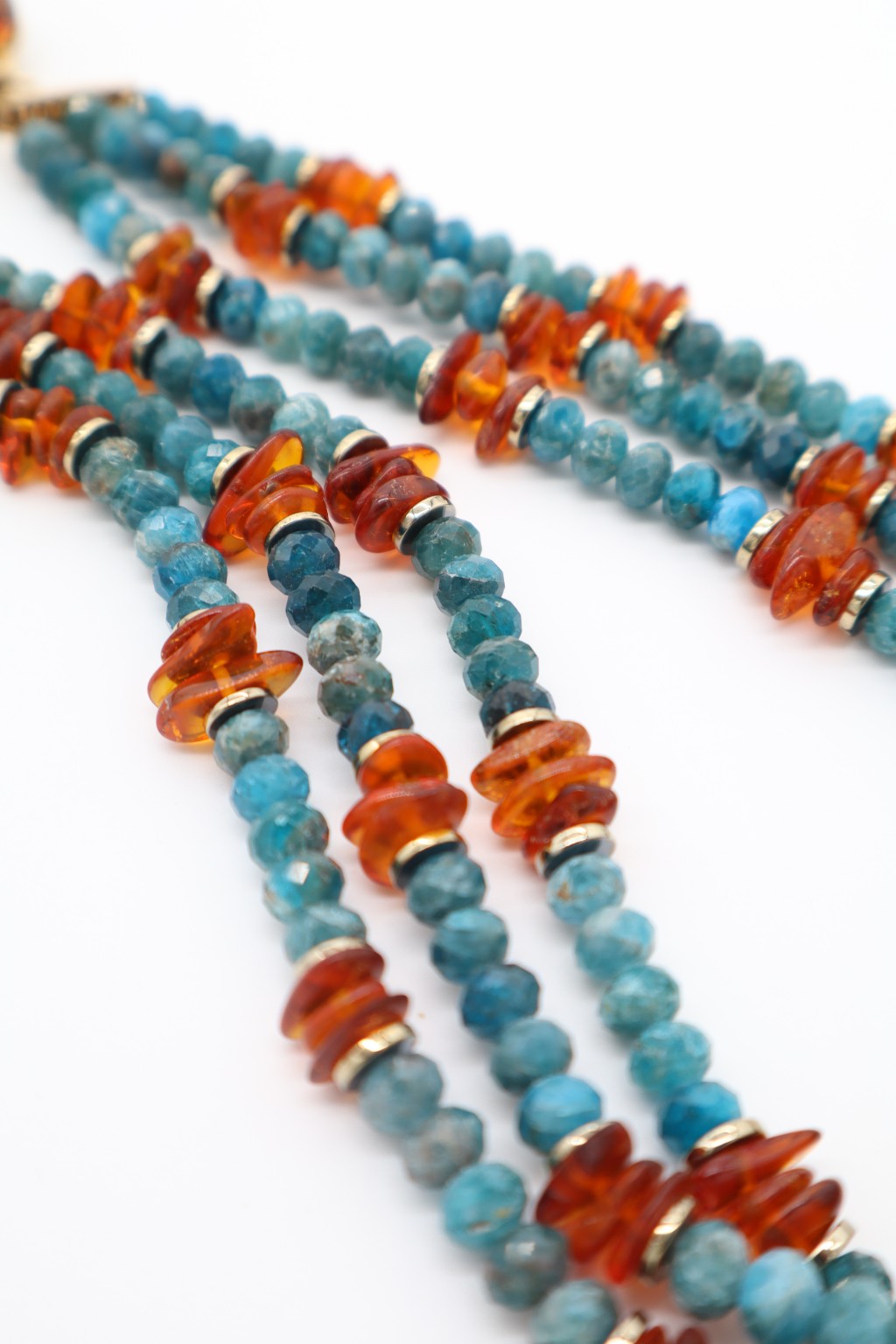 Dettaglio dei tre fili di apatite blu sfaccettata e degli elementi in ambra della collana