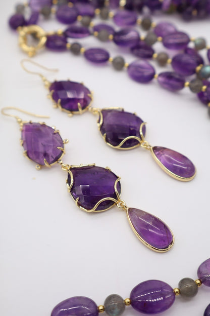Orecchini pendenti in ametista sfaccettata fotografati insieme a una collana in pietre naturali viola, suggerendo un possibile abbinamento coordinato.