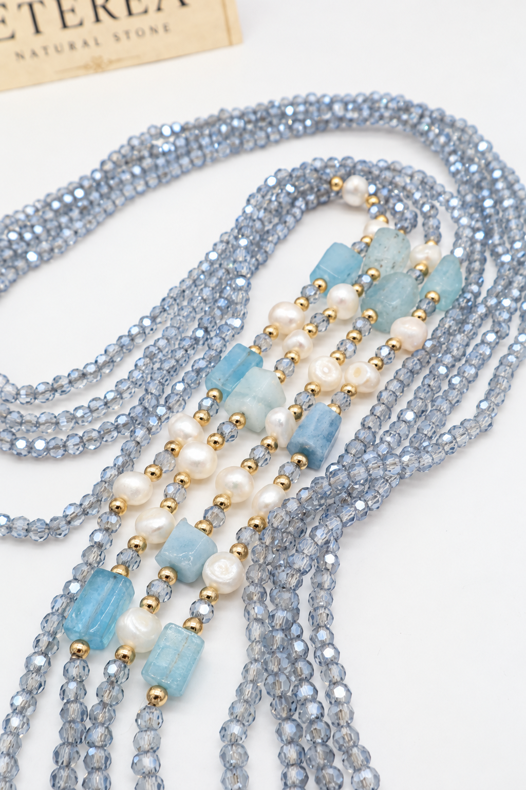 Collana multifilo azzurra da 90 cm con cristalli sfaccettati, acquamarina rettangolare da circa 12 × 8 mm, perle semi-round da 5 mm e distanziatori dorati.