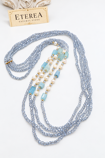 Collana multifilo azzurra da 90 cm con cristalli sfaccettati, acquamarina rettangolare da circa 12 × 8 mm, perle semi-round da 5 mm e distanziatori dorati.