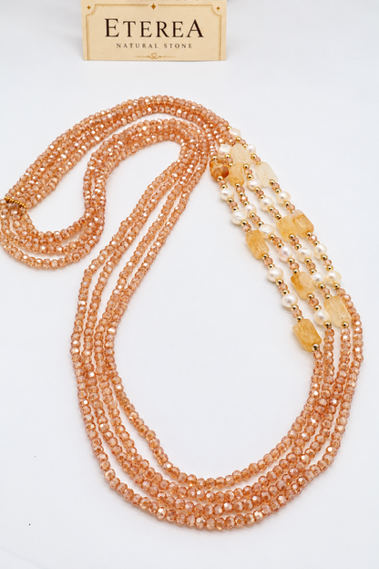 Collana multifilo da 90 cm con cinque fili di cristalli sfaccettati color champagne da 3 mm, citrino rettangolare da 14 × 10 mm, perle semi-round da 5 mm e distanziatori dorati.